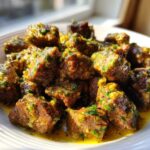 Close-up of tender, cubed crockpot steak pieces coated in a rich, yellow garlic butter sauce with visible green herbs.