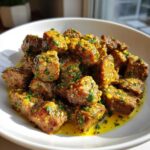 Close-up of tender crockpot steak bites coated in a rich, yellow garlic butter sauce and topped with fresh parsley.