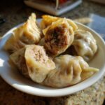 Close-up of steamed and pan-fried Traditional Chinese Dumplings, one cut open showing the savory meat filling.