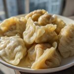 A close-up of several freshly steamed Traditional Chinese Dumplings piled high on a white plate.