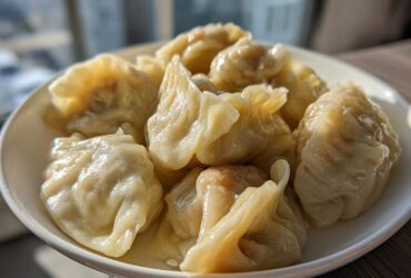 A close-up of several freshly steamed Traditional Chinese Dumplings piled high on a white plate.