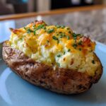 Close-up of a single, perfectly stuffed twice baked potatoes topped with melted cheddar cheese and fresh chives.