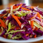 Close-up of a vibrant cabbage salad featuring shredded red cabbage, green cabbage, and bright orange carrots.