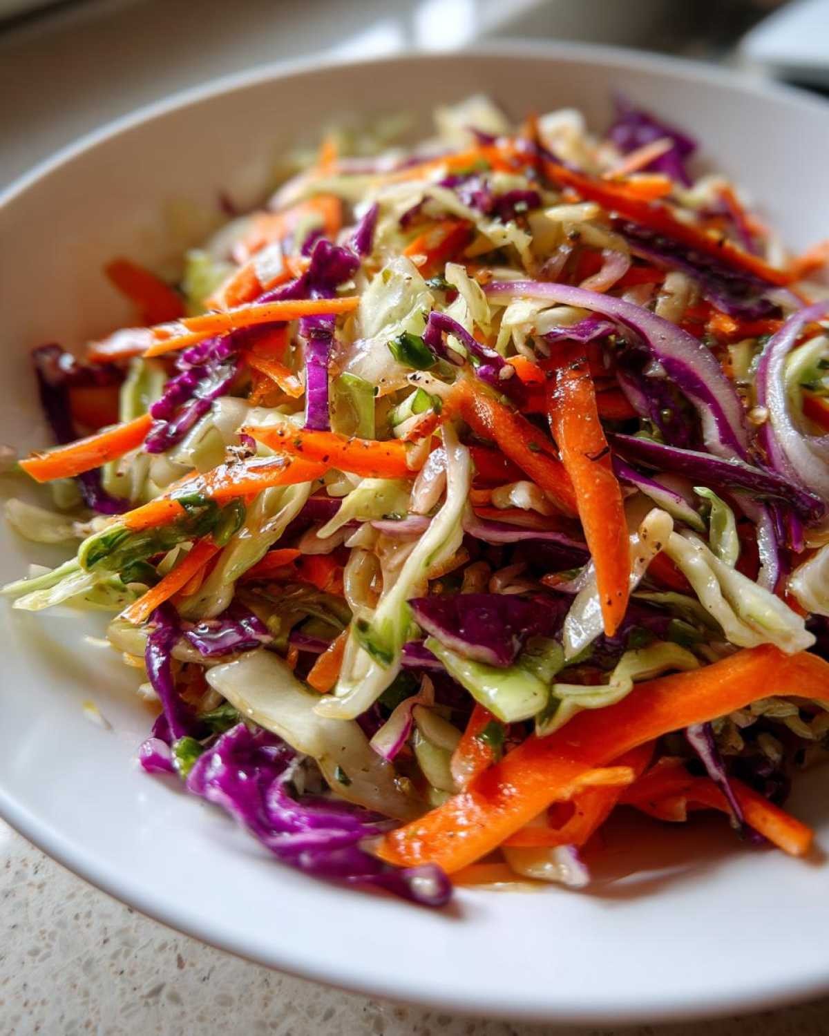 Close-up of a vibrant cabbage salad featuring shredded green cabbage, purple cabbage, carrots, and red onion tossed in a light dressing.