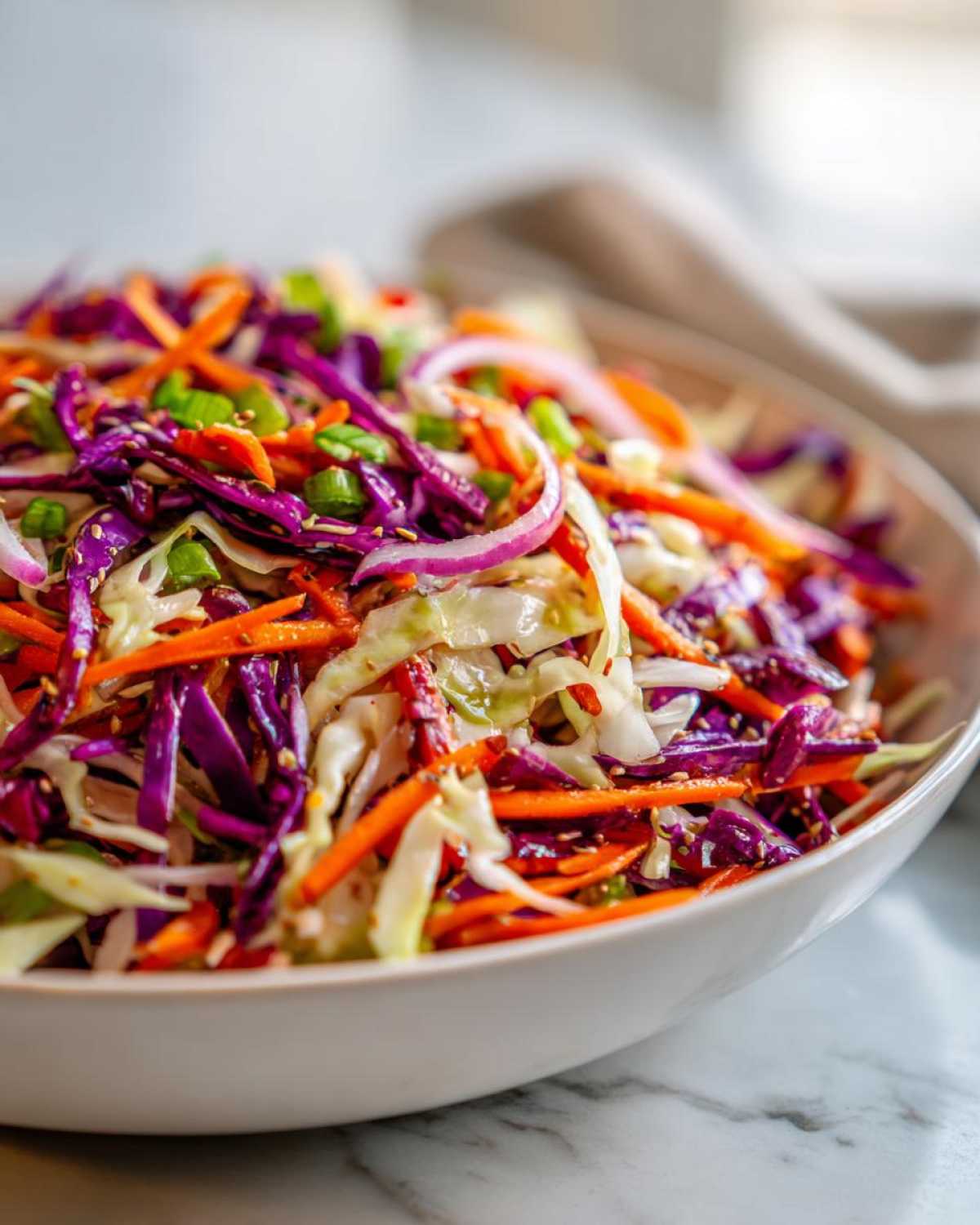 Close-up of a vibrant cabbage salad featuring shredded red and green cabbage, carrots, red onion, and sesame seeds.