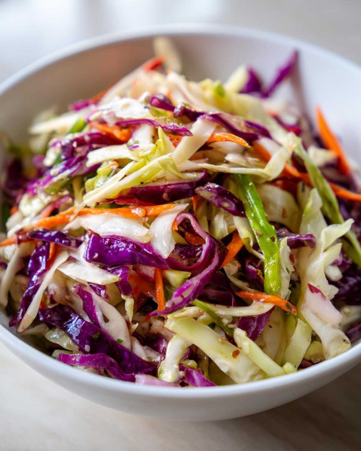 Close-up of a vibrant cabbage salad featuring shredded red and green cabbage and carrots in a white bowl.