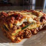 A thick, layered slice of zucchini lasagna featuring zucchini noodles, rich meat sauce, and melted mozzarella cheese topping.