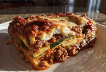 A thick, layered slice of zucchini lasagna featuring zucchini noodles, rich meat sauce, and melted mozzarella cheese topping.