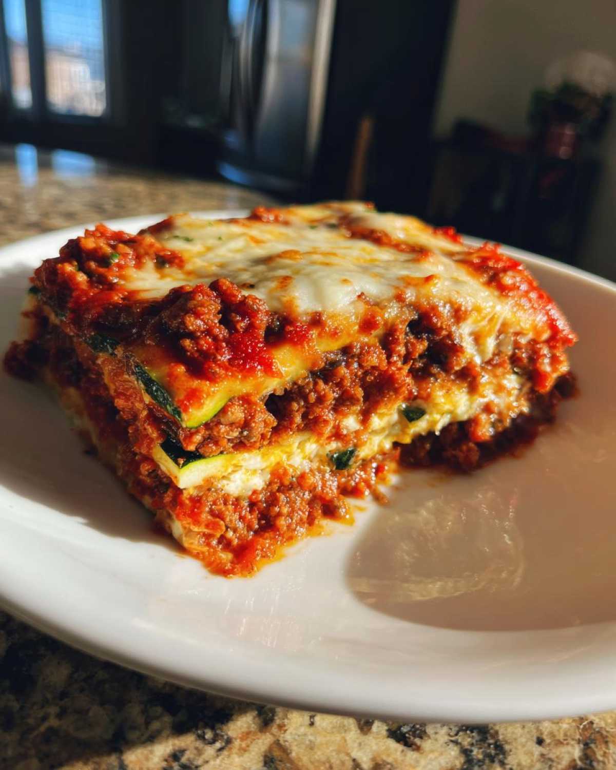 A single serving slice of zucchini lasagna, showing layers of meat sauce, ricotta, and zucchini noodles, topped with melted cheese.