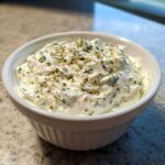 A white fluted bowl filled with creamy 5-Minute Greek Yogurt Ranch Dip, topped with fresh dill and spices.