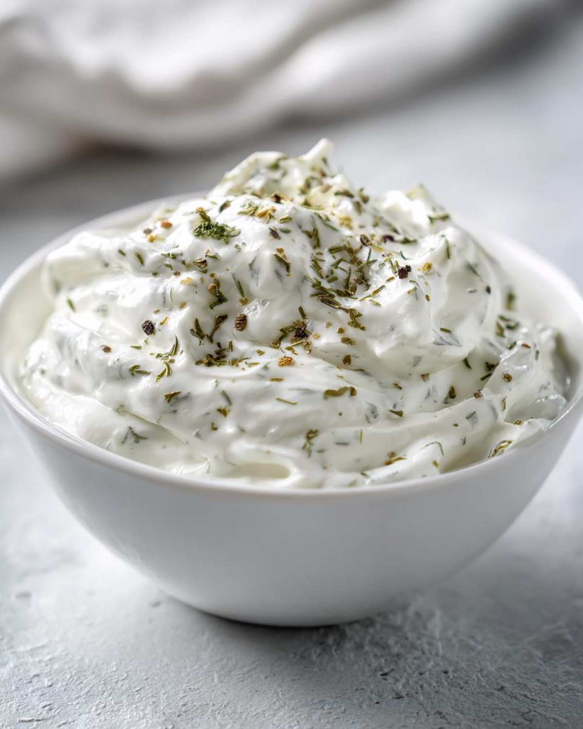 Close-up of thick, creamy 5-Minute Greek Yogurt Ranch Dip topped with dried herbs and spices in a white bowl.
