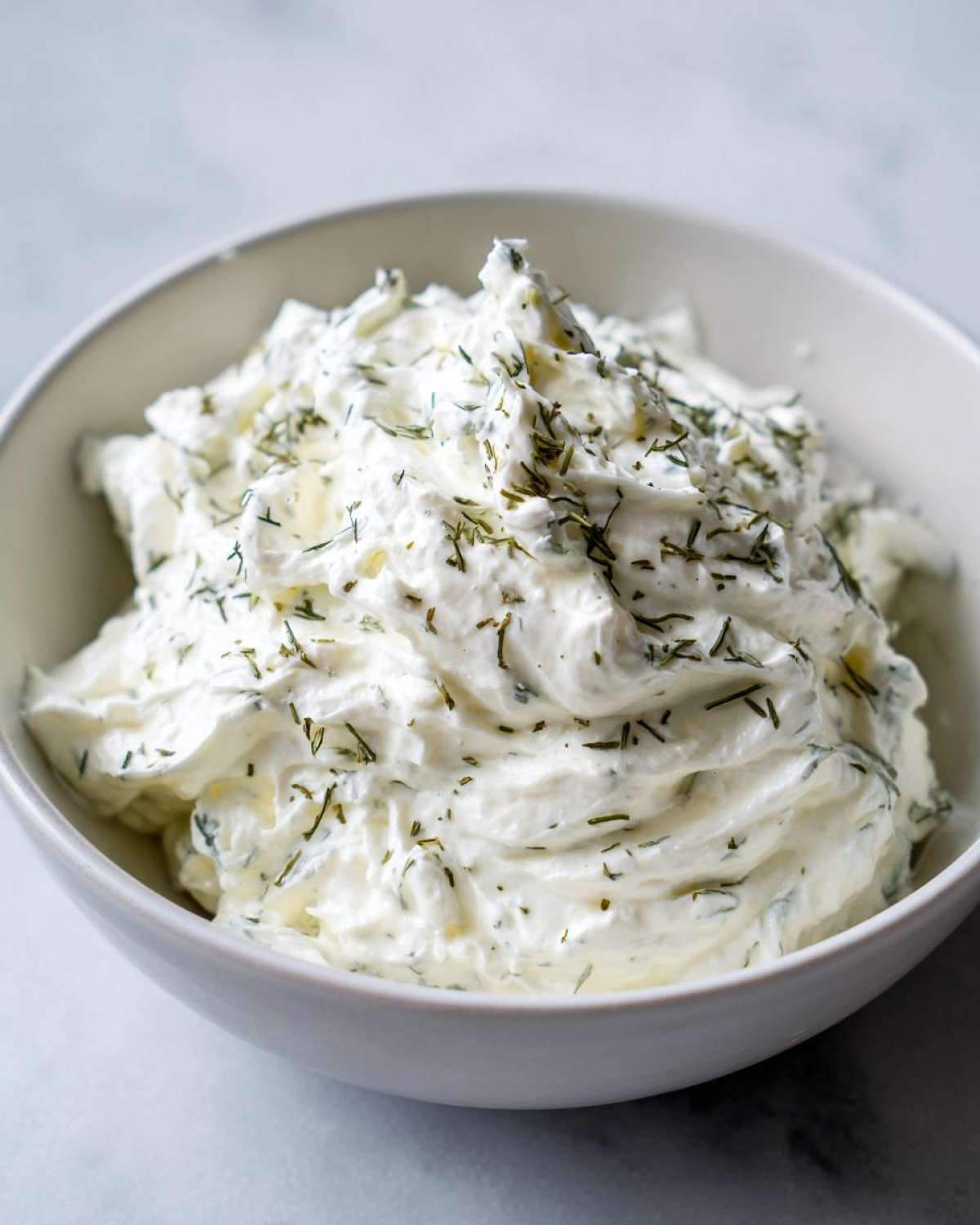 Close-up of thick, creamy 5-Minute Greek Yogurt Ranch Dip topped generously with chopped green herbs like dill.