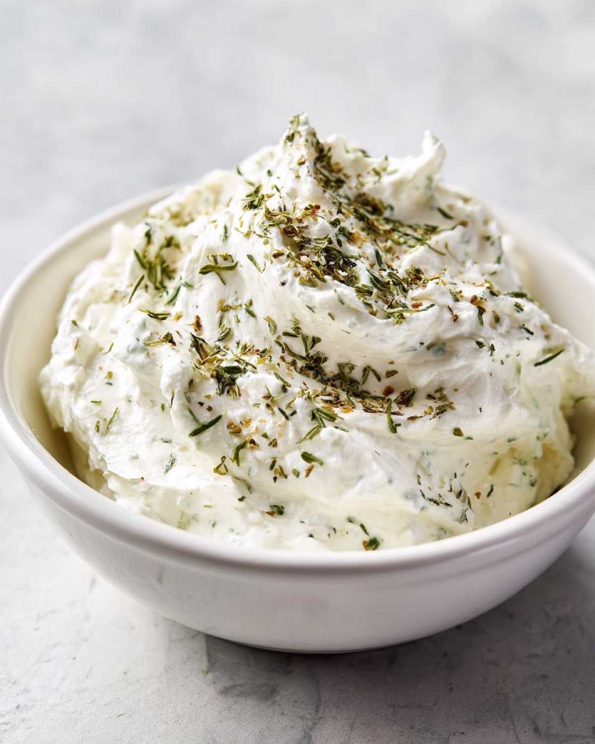 Close-up of thick, creamy 5-Minute Greek Yogurt Ranch Dip topped with dried herbs in a white bowl.
