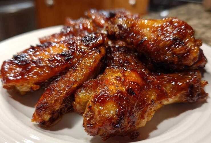 Close-up of several sticky, glazed Air Fryer BBQ Chicken Wings piled on a white plate.