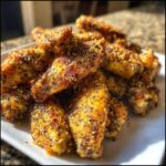 A close-up pile of crispy Air Fryer Lemon Pepper Wings generously coated in seasoning.