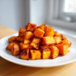 A mound of perfectly cooked, caramelized Air Fryer Sweet Potato Cubes piled high on a white plate.