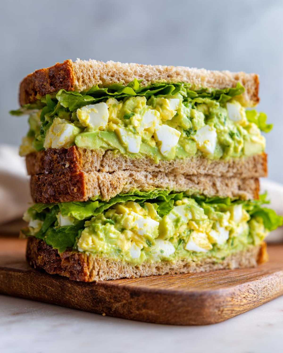 Close-up of a stacked Avocado Egg Salad Sandwich on whole wheat bread with lettuce.
