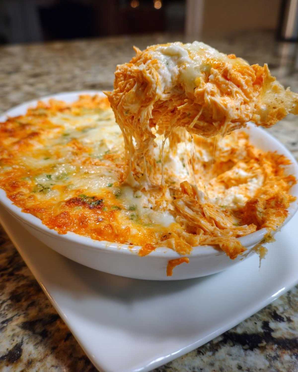 A chip loaded with stringy, cheesy Baked Buffalo Chicken Dip being pulled from a white serving dish.