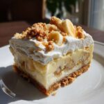 A rich, layered slice of Banana Pudding Cheesecake Bars topped with whipped cream, banana slices, and cookie crumbs.