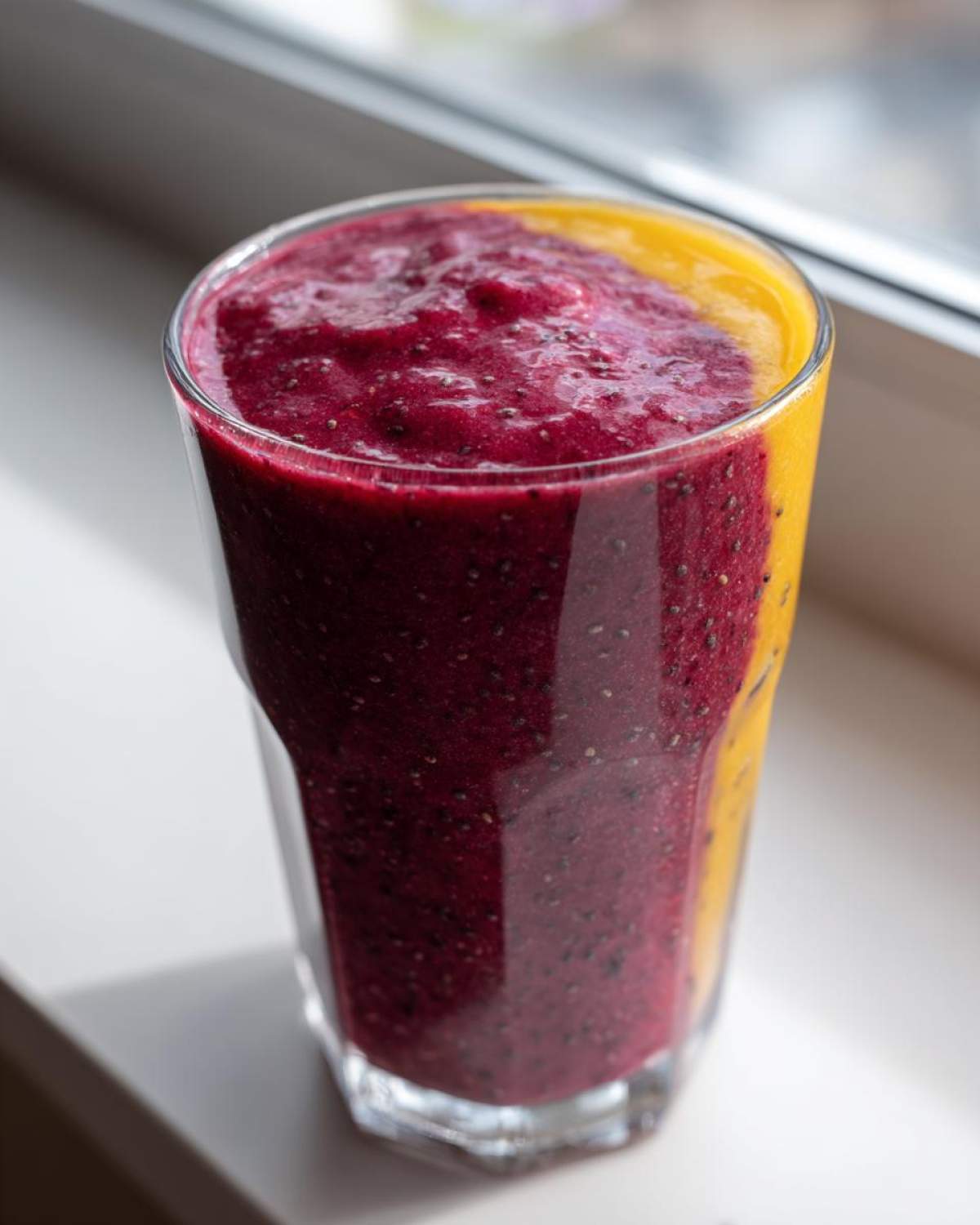 Close-up of a layered smoothie featuring a deep magenta berry layer and a bright yellow layer, showing visible chia seeds in the Blueberry Lemon Chia Smoothie.