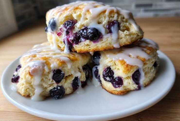 Three delicious Blueberry Lemon Scones stacked on a white plate, generously drizzled with white lemon glaze.