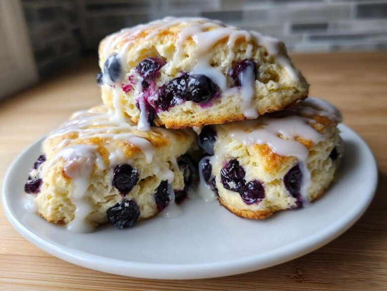Three delicious Blueberry Lemon Scones stacked on a white plate, generously drizzled with white lemon glaze.