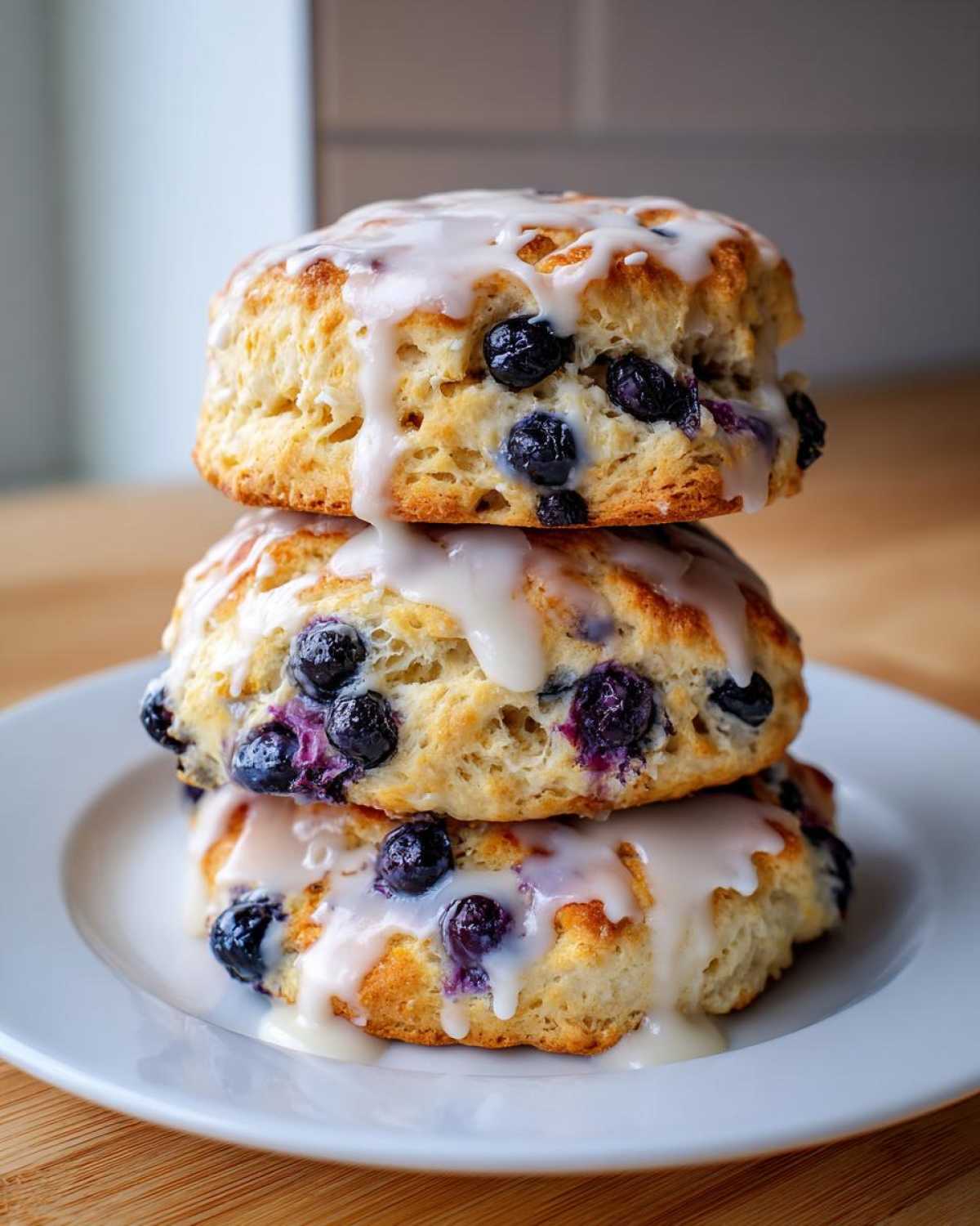 Three stacked Blueberry Lemon Scones drizzled with a thick white glaze on a white plate.