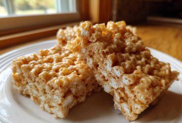 Two squares of gooey Brown Butter Rice Krispie Treat Bars stacked slightly on a white plate.