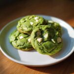 Four vibrant green Chewy Matcha White Chocolate Cookies studded with white chocolate chunks on a white plate.