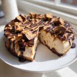 A slice removed from a rich Chocolate Peanut Butter Cheesecake Dip topped with chocolate and peanut butter drizzles and Reese's pieces.