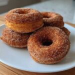 A stack of four freshly made Cinnamon Sugar Air Fryer Donuts coated heavily in cinnamon sugar mix.