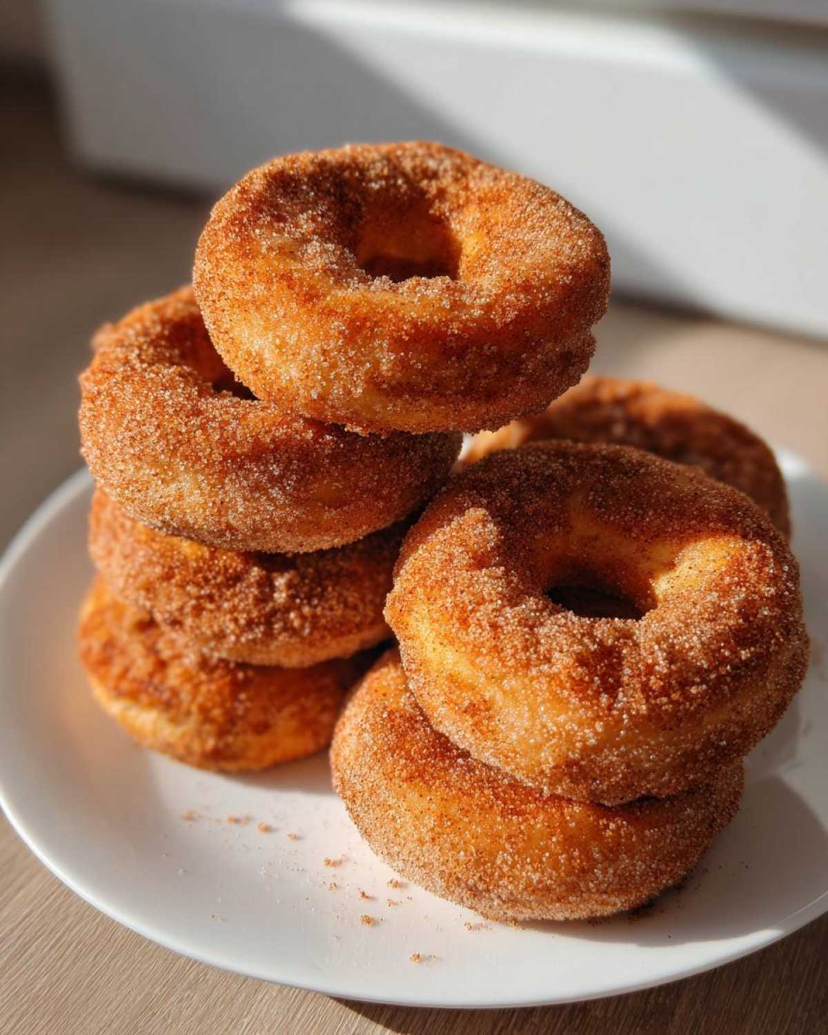 A stack of golden brown Cinnamon Sugar Air Fryer Donuts heavily coated in cinnamon sugar, resting on a white plate.