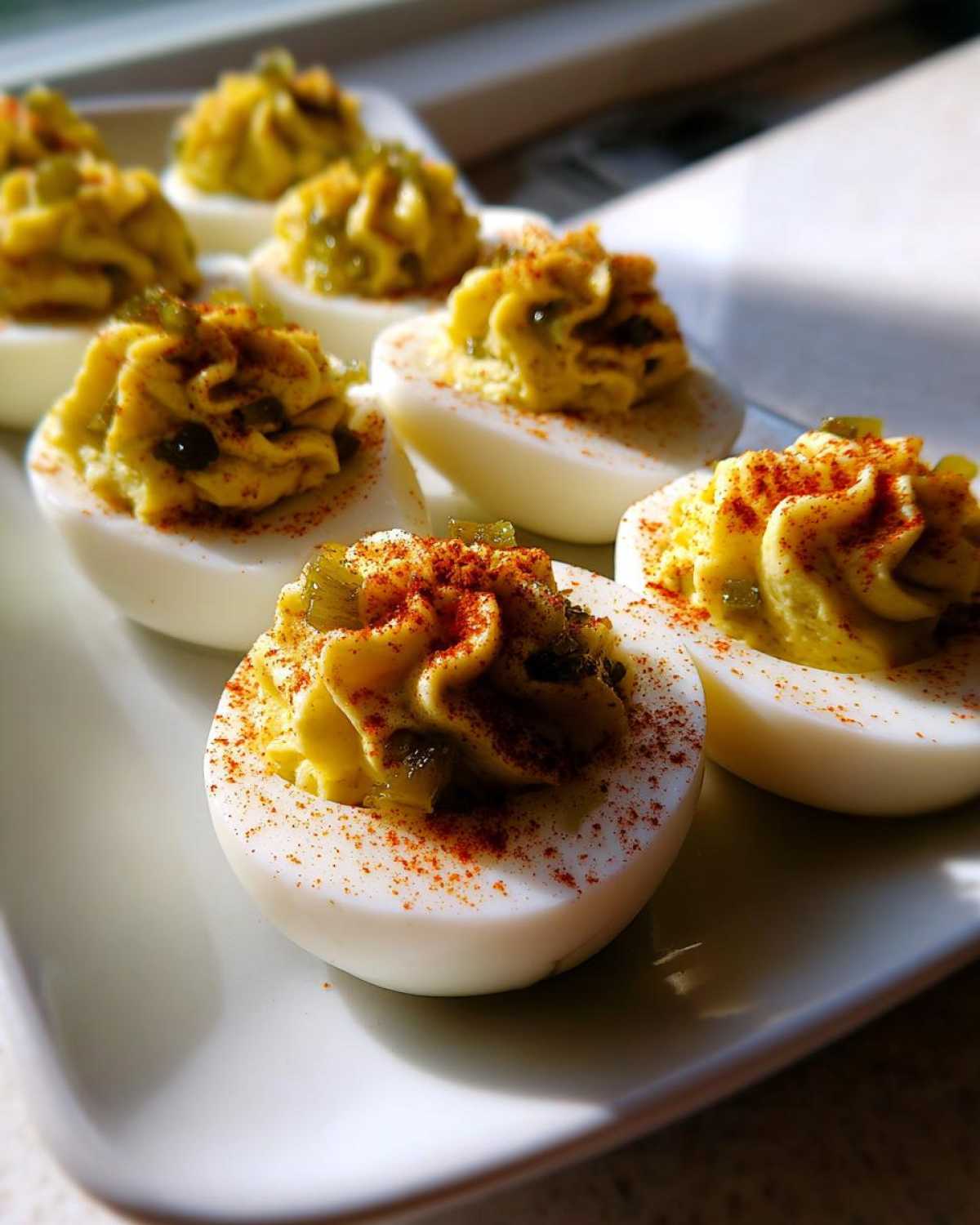 Close-up of Classic Deviled Eggs with Dill Pickle Relish piped high and sprinkled with paprika on a white platter.