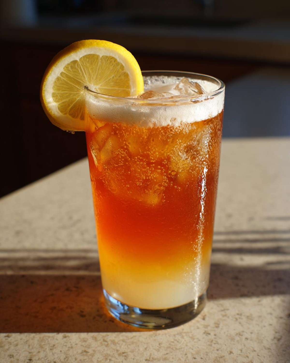 A tall glass filled with layered Cold Brew Lemonade, ice, foam, and a fresh lemon slice garnish.