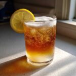 A tall glass of bubbly Cold Brew Lemonade garnished with a fresh lemon slice, sitting in sunlight.