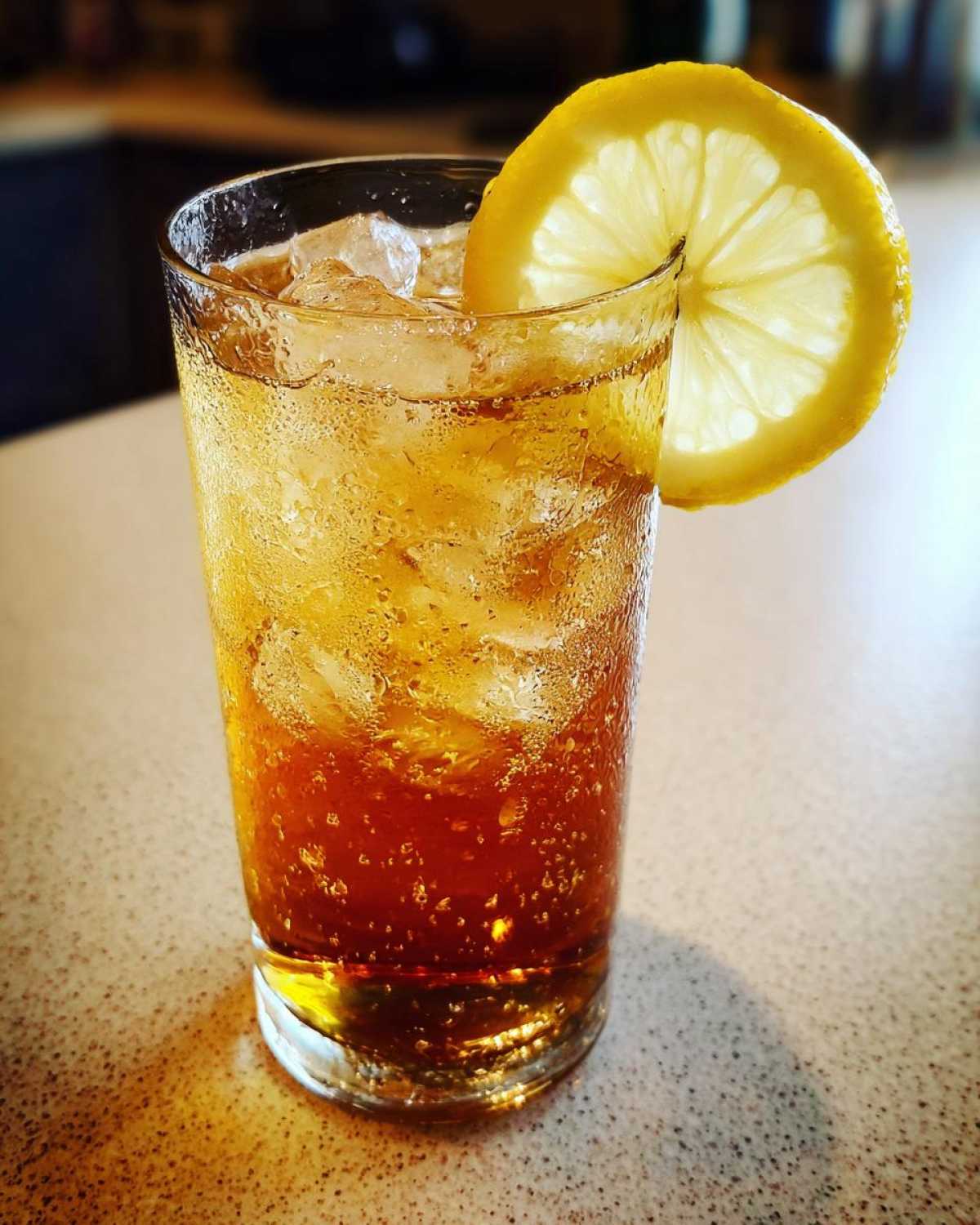A tall glass filled with ice and amber-colored Cold Brew Lemonade, garnished with a bright lemon slice.