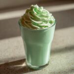 A tall glass filled with a light green Copycat Shamrock Shake topped with a swirl of mint whipped cream.