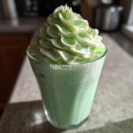 A tall glass of bright green Copycat Shamrock Shake topped with a swirl of mint whipped cream.
