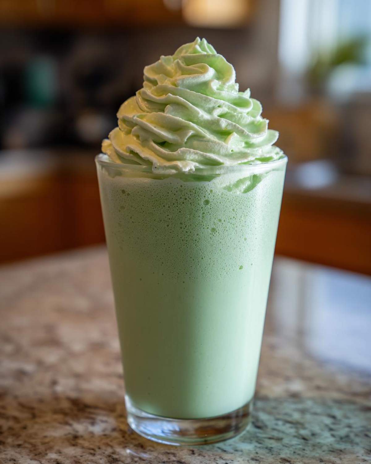 A tall glass filled with a light green Copycat Shamrock Shake topped with a swirl of mint whipped cream.