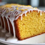Close-up of a moist Copycat Starbucks Iced Lemon Loaf with thick white glaze dripping down the side and lemon zest on top.