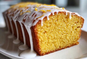 Close-up of a moist Copycat Starbucks Iced Lemon Loaf with thick white glaze dripping down the side and lemon zest on top.