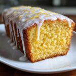 A moist slice of Copycat Starbucks Iced Lemon Loaf with thick white glaze dripping down the sides and lemon zest on top.