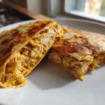 Two halves of a golden-brown quesadilla filled with shredded chicken coated in Copycat Taco Bell Chicken Quesadilla Sauce.