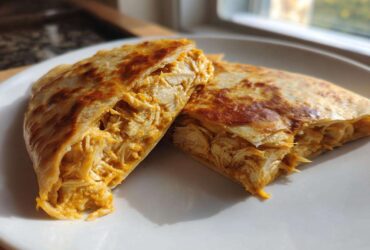 Two halves of a golden-brown quesadilla filled with shredded chicken coated in Copycat Taco Bell Chicken Quesadilla Sauce.