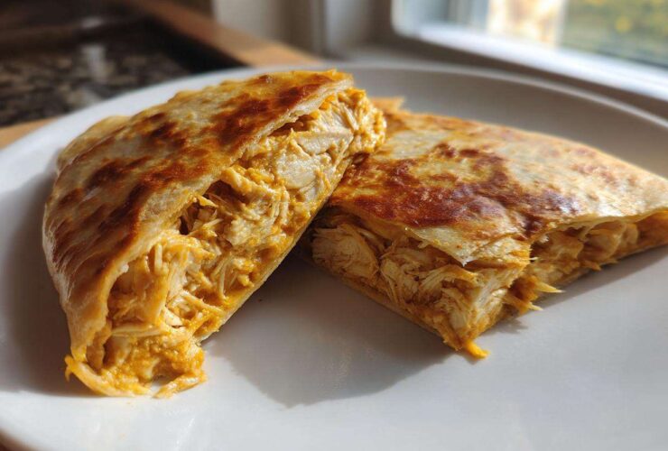 Two halves of a golden-brown quesadilla filled with shredded chicken coated in Copycat Taco Bell Chicken Quesadilla Sauce.