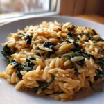 A close-up of a serving of Creamy Garlic Parmesan Orzo with Spinach on a white plate.