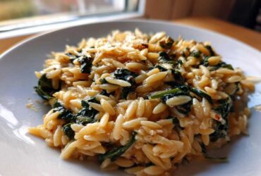 A close-up of a serving of Creamy Garlic Parmesan Orzo with Spinach on a white plate.