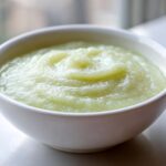 Close-up of a white bowl filled with smooth, light green Creamy Potato Leek Soup.