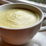 Close-up of a white mug filled with smooth, light green Creamy Potato Leek Soup.