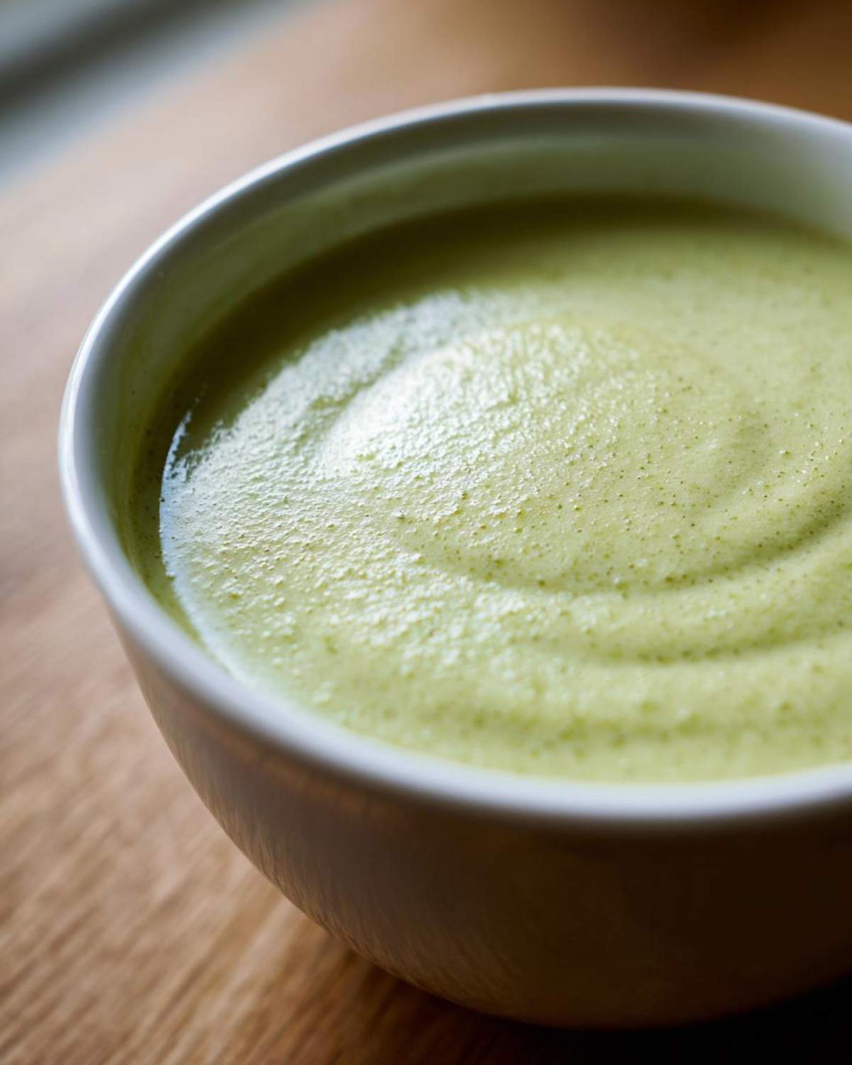 Close-up shot showing the smooth, pale green texture of Creamy Potato Leek Soup in a white bowl.